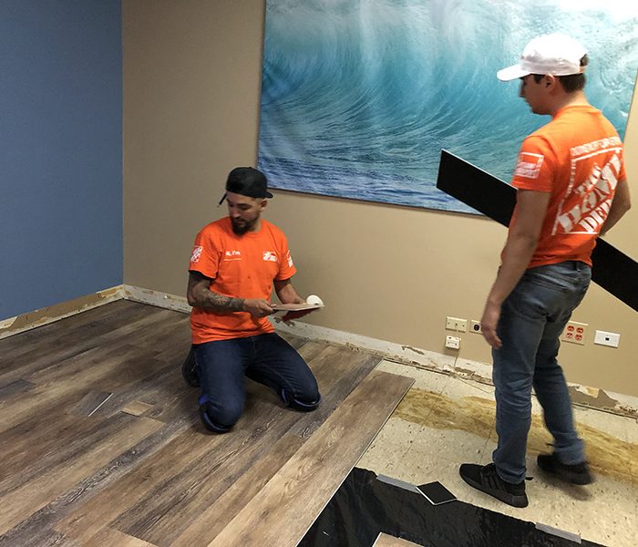 Luis Banuelos, kneeling, accepts a plank of flooring to be installed in the kids room at the Homewood Cancer Support Center. This was the one room being worked on inside the building. (Marilyn Thomas/H-F Chronicle)