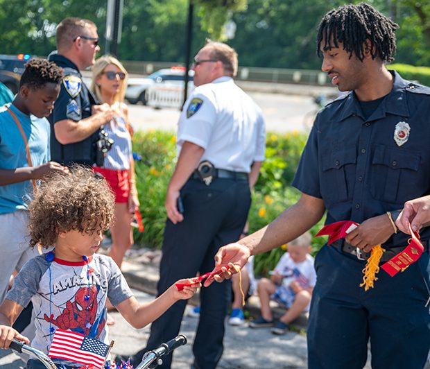 july4parade_220704_10 Flossmoor firefighter and E.M.T. Shamarr Shelton, right, hands a ribbon to Christian Young in downtown Flossmoor after the 4th of July parade. (ABS)
