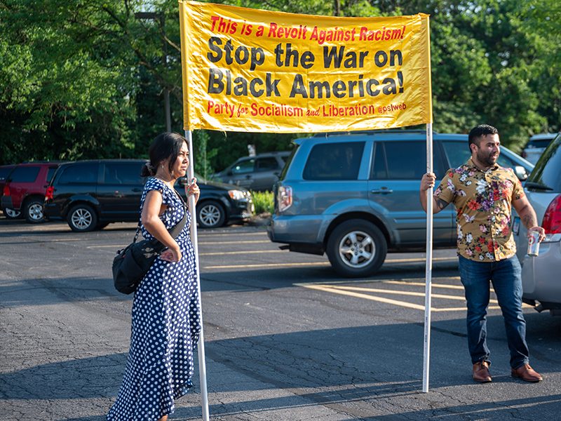 Candice Choo-Kang and Shabbir Rizvi of the Party for Socialism and Liberation (PSL) hold a banner that reads "Stop the War on Black America!" outside of Flossmoor village hall on Monday, July 18. (Andrew Burke-Stevenson/H-F Chronicle)