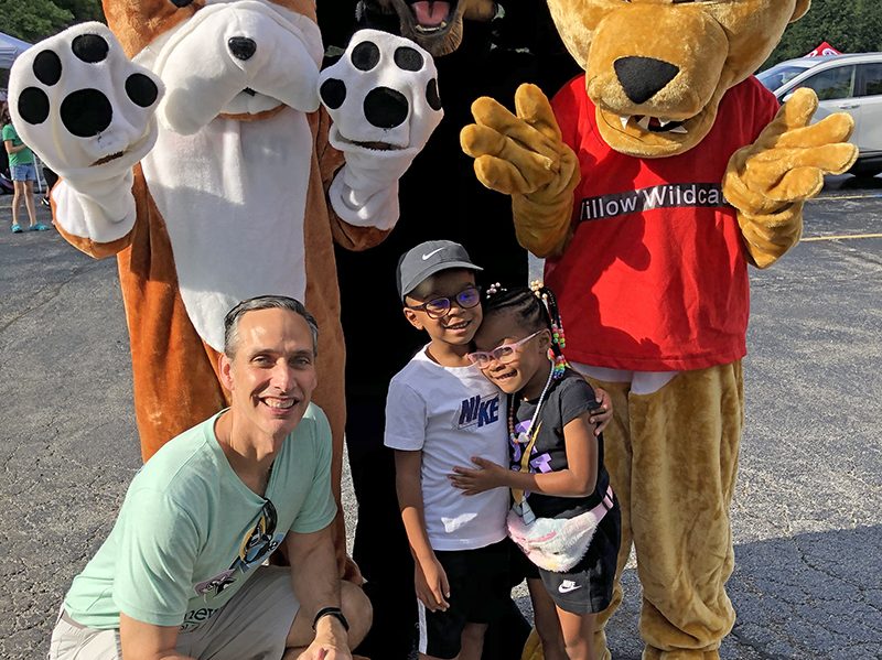 District 153 Superintendent Scott McAlister gets down to greet Michael Mayfield Jr., a first grader, and sister Averie Mayfield, a kindergartener, at Willow School. They were greeted by school mascots (standing, from left) Churchill Bulldog, James Hart Panther and Willow Wildcat. (Marilyn Thomas/H-F Chronicle)