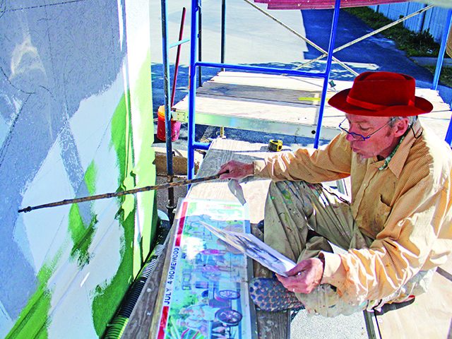 Thomas Melvin consults a design drawing while painting "Independence Day," the mural on the south wall of the former Mama & Me Pizza building. (Eric Crump/H-F Chronicle)