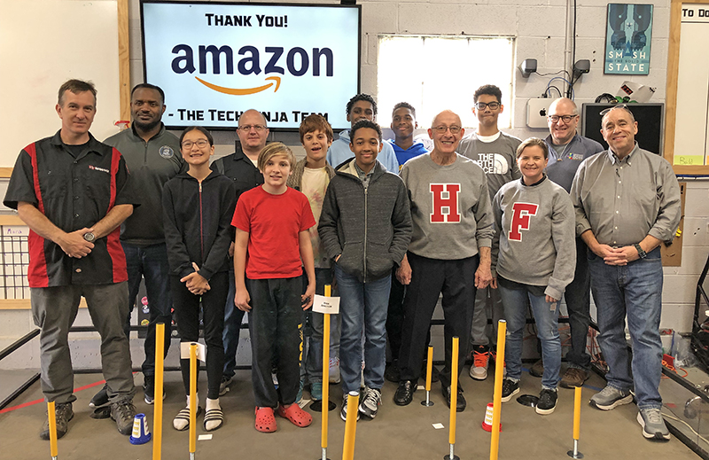 Lamonte Heyward, left in back row, general manager of the Amazon Distribution Center in Matteson, came to a meeting of the HF Robotics team in October to present them with $3,000 in new equipment. He is pictured with team members, coaches, members of the Homewood Science Center board and Homewood Mayor Rich Hofeld and Flossmoor Mayor Michelle Nelson (front row with H-F sweatshirts). (Marilyn Thomas/H-F Chronicle)