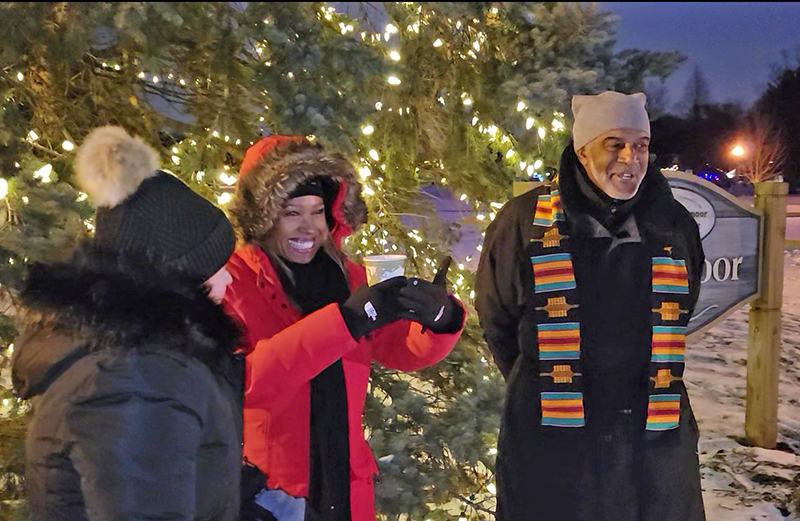 Felecia Lofton, middle, gives a thumbs up as the crowd at the first night of Kwanzaa in Flossmoor cheers following Mayor Michelle Nelson's introduction of her and her husband, Trustee George Lofton, right. (Eric Crump/H-F Chronicle)