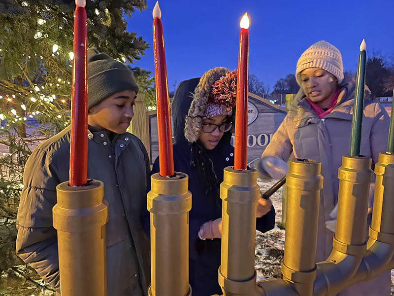 Gregory and Kathleen Mitchell light two candles on the kinara, one black and one red, on the second night of Kwanzaa, as their mother Kimberly watches at Flossmoor Park. (Bill Jones/H-F Chronicle)