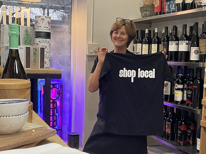 Maureen Mader, owner of Dunning’s Market & Deli, shows off a “shop local” T-shirt inside of her downtown Flossmoor space during the holiday open house. (Bill Jones/H-F Chronicle)
