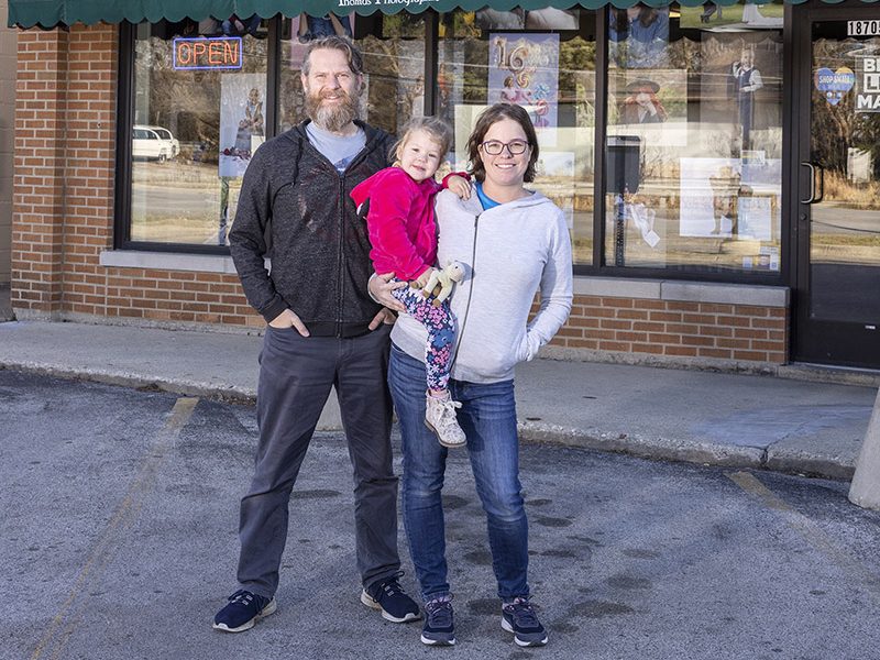 Thomas Photographic owners Colin, left, and Angela Thomas with their daughter, Elloren, in front of their current location at 18705 Dixie Highway. The couple currently is working to remodel space in a storefront across the street where they plan to move to in coming weeks. (Provided photo)
