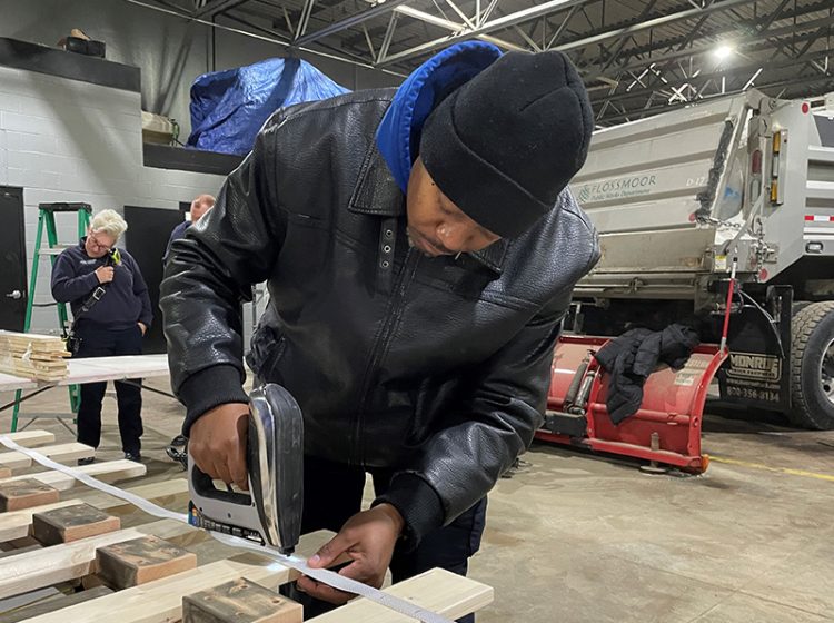 Police Officer Keith Hale staples a strip of fabric into a series of boards during Sleep in Heavenly Peace’s bed build at the Flossmoor Public Works garage. (Bill Jones/H-F Chronicle)