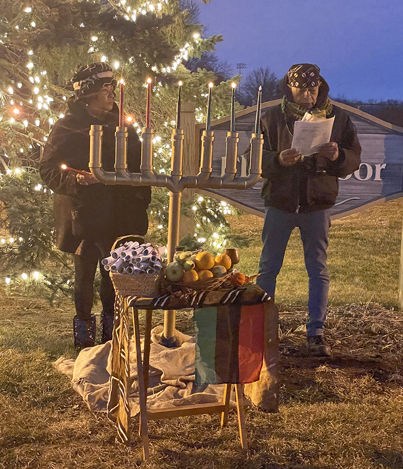 Leonard Harris, of Flossmoor, reads the daily principles of Kwanzaa as his wife, Donna, lights each candle on the community kinara at Flossmoor Park. (Bill Jones/H-F Chronicle)
