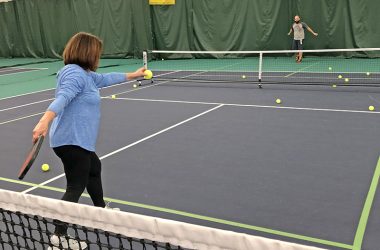 Monica Zackary practices her pickleball serves at the H-F Racquet & Fitness Club. Two pickleball courts are made from one tennis court. The net in the foreground is a tennis net. (Marilyn Thomas/H-F Chronicle)