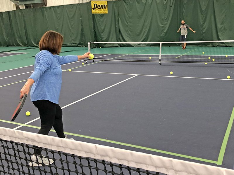 Monica Zackary practices her pickleball serves at the H-F Racquet & Fitness Club. Two pickleball courts are made from one tennis court. The net in the foreground is a tennis net. (Marilyn Thomas/H-F Chronicle)