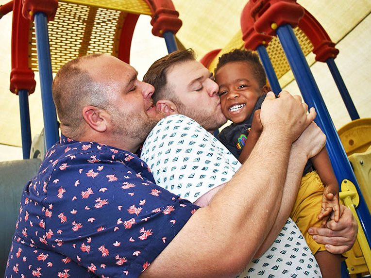 Rowan Willard-Rose gets a big hug from his dads, J.R., left, and Brandon Willard-Rose. (Mary Compton/H-F Chronicle)