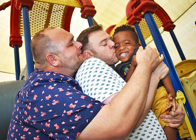 Rowan Willard-Rose gets a big hug from his dads, J.R., left, and Brandon Willard-Rose. (Mary Compton/H-F Chronicle)