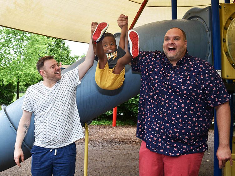 Rowan Willard-Rose, center, gets a “dad swing” from his dads, J.R., right, and Brandon, left. (Mary Compton/H-F Chronicle)