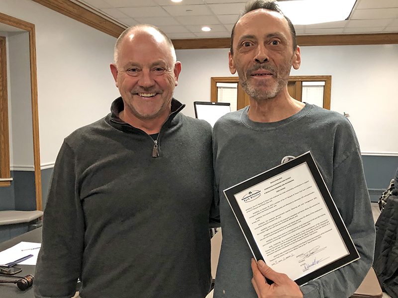 Brent Bachus, left, president of the Homewood-Flossmoor Park District Board of Commissioners, presents Christopher Demski, a staff member at the H-F Racquet & Fitness Center, a plaque recognizing his efforts that saved the life of a patron. (Marilyn Thomas/H-F Chronicle)