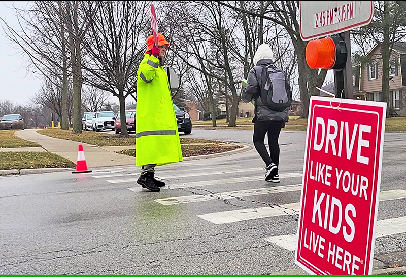 Crossing guard Sandy Byron helps a Heather Hill School student cross Lawrence Crescent on Feb. 16. Byron has asked Flossmoor officials to install stop signs at the corner to help control speeding drivers. (Eric Crump/H-F Chronicle)