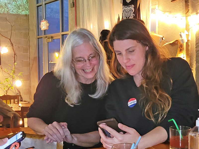 Homewood trustee candidate Anne Colton, left, looks on as Sarah Meeks checks election results on her phone during a results watching party at Rabid Brewing on Tuesday evening. (Eric Crump/H-F Chronicle)