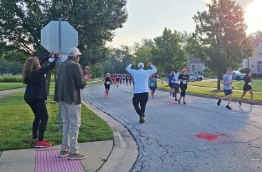 Flossmoor Trustree George Lofton, with arms raised, and his wife, Felecia, far left, along with Ballantrae Neighborhood Watch Captain Les Rodgers, left, cheer on the runners. (Jalyn Edwards/H-F Chronicle)