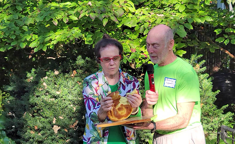 Gloria Lippert breaks bread as part of the Sukkot ceremony while her husband, Jeffery Lippert, speaks to the diverse group of friends and family at the event Oct. 1 in Flossmoor.