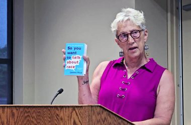 Jackie Riffice holds up a copy of "So You Want to Talk About Race" by Ijeoma Oluo as she announces a new community book club, Books Without Borders, at the July 8 Homewood board meeting. (Eric Crump/H-F Chronicle)