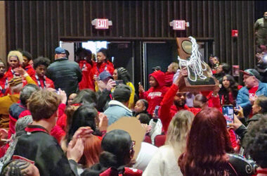 The state champion H-F High boys basketball team enters Mall Auditorium following their coach, Jamere Dismukes, trophy held high, for a celebration Sunday, March 10, of the team's accomplishments. (Eric Crump/H-F Chronicle)