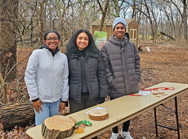 From left, students Victoria Plummer, Mariah M., and Andrew Johnson earn some volunteer hours for helping people determine the age of a maple tree and teaching them which trees are old enough for tapping. (Chris Weber/H-F Chronicle)