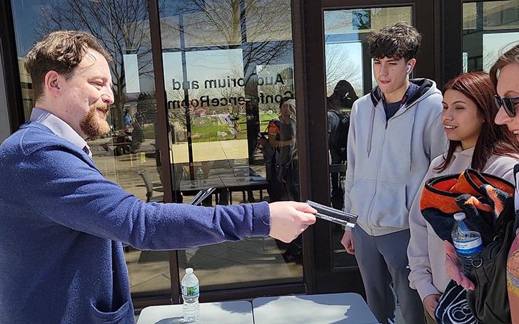 Russell Guldin, left, hands out eclipse glasses in the courtyard at Prairie State College on April 8. (Eric Crump/H-F Chronicle)