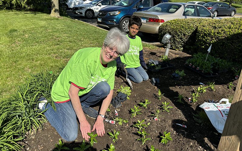 Debbie Maxwell works alongside Iranian Mitra Samaddar in the flower bed at Patriots Park in Homewood. (Marilyn Thomas/H-F Chronicle)