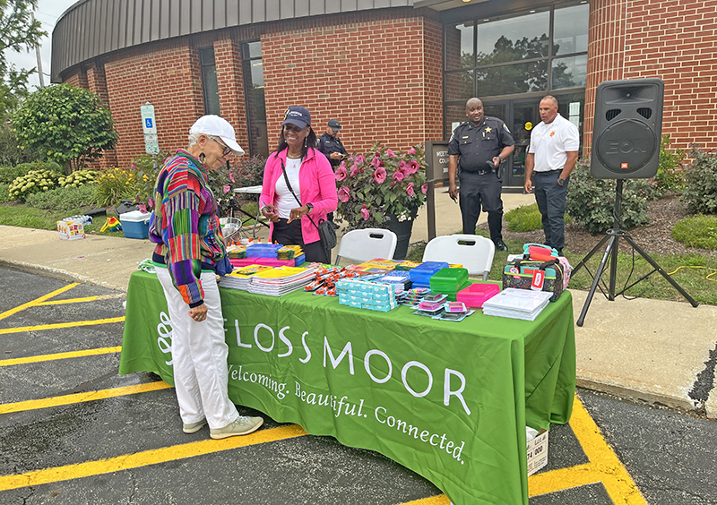 Flossmoor Trustee Rosalind Mustafa stops at the table tended by Community Relations Commission Chairwoman Phillipa Leon-Thompson with freebies for guests that were donated by Meijers. (Nuha Abdessalam/H-F Chronicle)