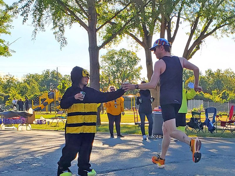 Zach Humm hands Gatorade to a passing runner at the Hidden Gem's Heather Hill water station. (Chris Weber/H-F Chronicle)