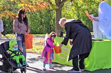 H-F Park District official Bob Birgel offers a bucket of candy to Melida Koyn while her parents, Kandy and Jordan Koyn, and brother Leo look on. Park district staffer Steve Rab, the ghost, prepares to give the Koyns information about upcoming park district events. (Eric Crump/H-F Chronicle)