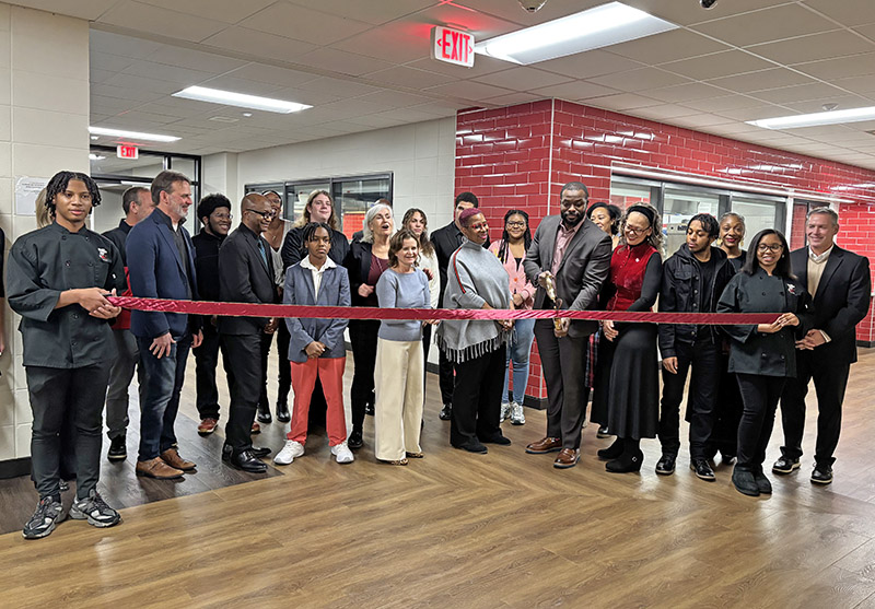 A crowd of students, District 233 school board members and administrators and special guests gathered around Principal Clinton Alexander, with scissors, as he prepares to cut the ribbon officially opening the new culinary, fashion design and interior design wing at Homewood-Flossmoor High School's North Building on Dec. 17. (Marilyn Thomas/H-F Chronicle)