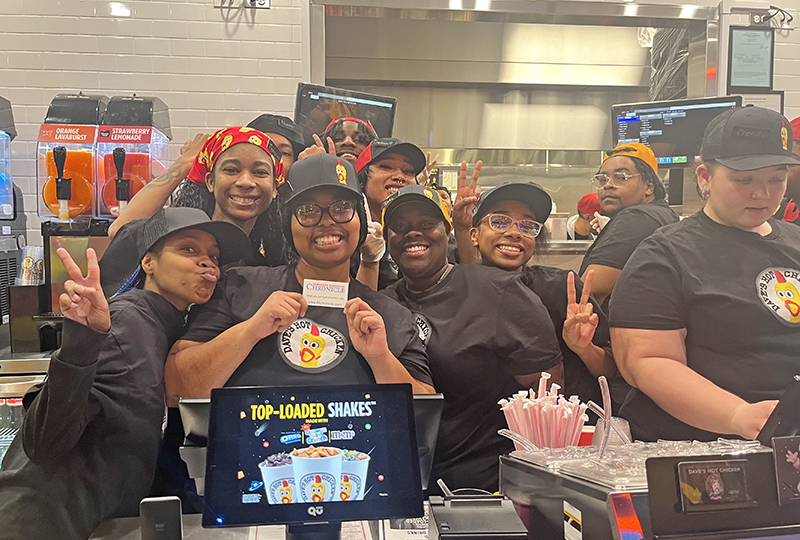 Dave’s Hot Chicken employees pose for the camera and hold up a Homewood-Flossmoor Chronicle business card at private event for friends, family and the media on Jan. 29. (Nick Ulanowski/H-F Chronicle)