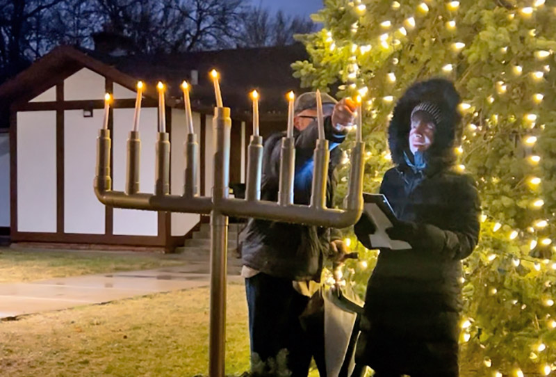 Larry Burrows lights the menorah alongside his wife, Nancy Burrows, who spoke about their family traditions celebrating Hanukkah. (Faith Lee/H-F Chronicle)