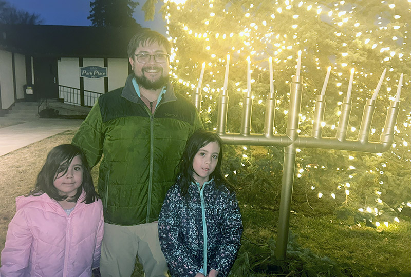 Jacob Schoeneman of Flossmoor alongside his two daughters after lighting the menorah on Dec. 30. (Faith Lee/H-F Chronicle)