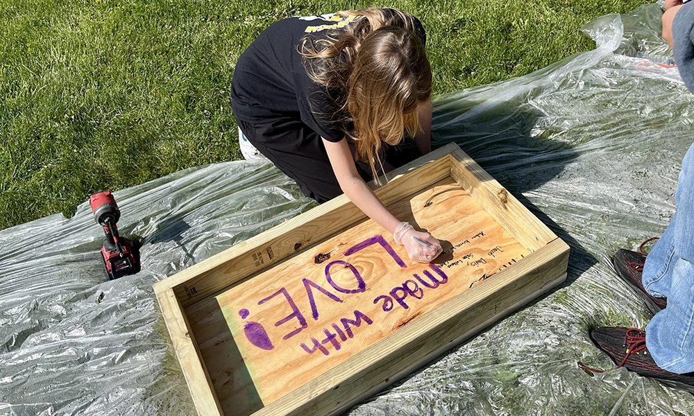 Gemma Davis signs her name on the bottom of a pantry box — a special touch encouraged by Korey Ziemkowski so every child could leave their mark on the project. (Nuha Abdessalam/H-F Chronicle)