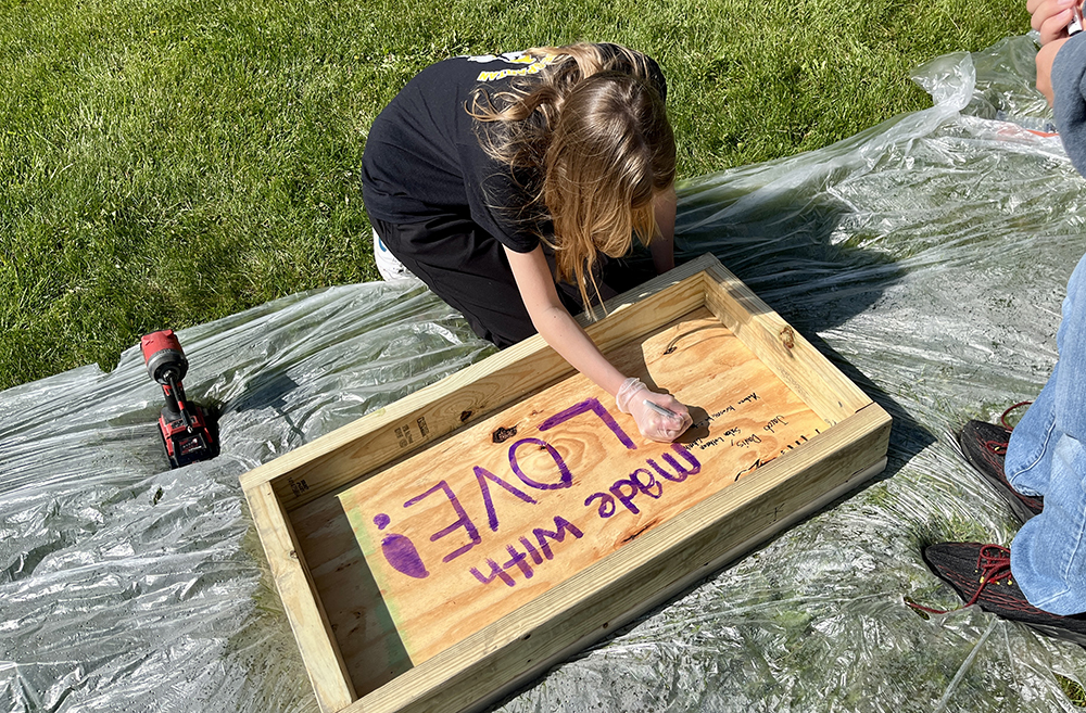 Gemma Davis signs her name on the bottom of a pantry box — a special touch encouraged by Korey Ziemkowski so every child could leave their mark on the project. (Nuha Abdessalam/H-F Chronicle)