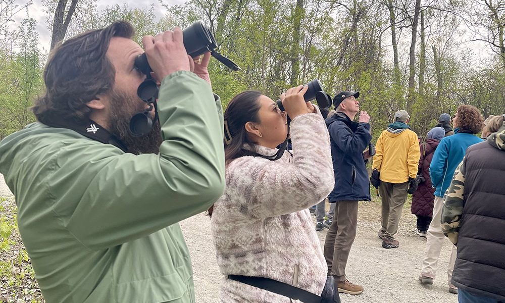World Migratory Bird Day attendees at Izaak Walton Preserve use binoculars to scan for birds during a tour. (Summer Kiswani/ H-F Chronicle)