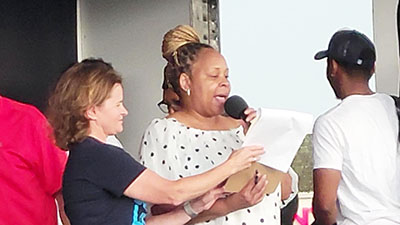 Flossmoor Mayor Michelle Nelson, left, helps keep notes from fluttering in a rising breeze as Chicago Southland Chamber of Commerce Director Jennel Hooper thanks sponsors of Chamber Night after announcing the event would need to end early because of lightning from a nearby thunderstorm. Behind them, crews begin packing up sound equipment. (Eric Crump/H-F Chronicle)