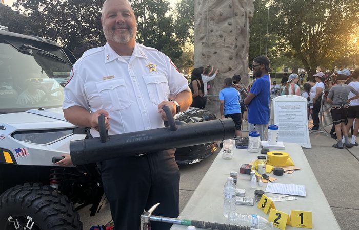 Homewood Deputy Police Chief Tom Johnson holds up a battering ram on display on a table at National Night Out. (Nick Ulanowski / H-F Chronicle)