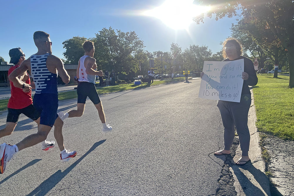 A volunteer from the South Suburban Vineyard Church holds up sign saying "I'm glad it's you and not me, you can do it! Ten miles to go!" (Jamilah Lewis/H-F Chronicle)