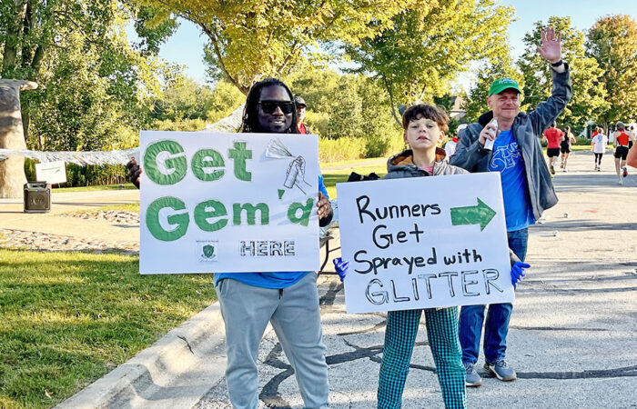 Nigel and Qadree Holmes hold signs and toss glitter as runners pass during the Hidden Gem Half Marathon in Flossmoor. (Nuha Abdessalam/H-F Chronicle)