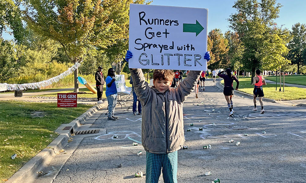 Nigel Holmes holds a sign to cheer on runners during the Hidden Gem Half Marathon in Flossmoor. (Nuha Abdessalam/H-F Chronicle)