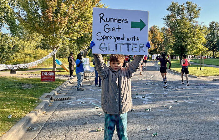 Nigel Holmes holds a sign to cheer on runners during the Hidden Gem Half Marathon in Flossmoor. (Nuha Abdessalam/H-F Chronicle)
