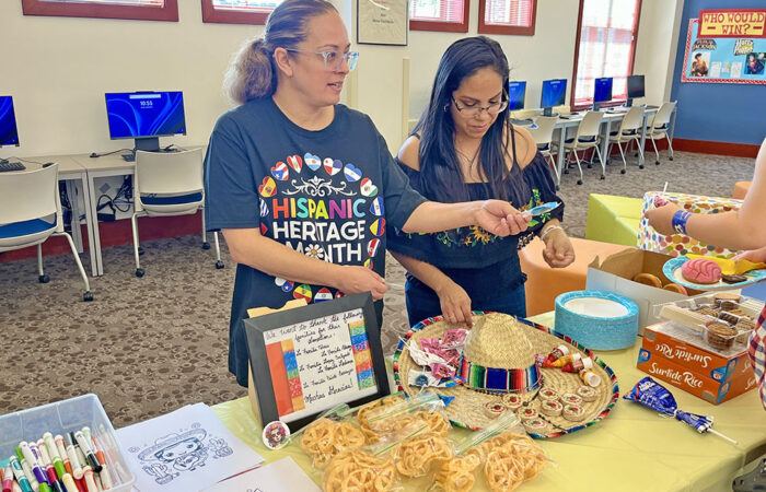 Gloria Prieto and Rosalinda Ledesma of BPAC help families at the game and snack table. (Nuha Abdessalam/H-F Chronicle)