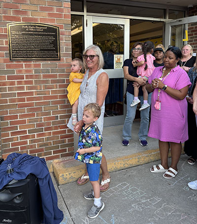 Retired District 153 school board member Shelly Marks stands with her grandchildren Ava and Jonah in front of the plaque letting all who pass that the playground at Willow School is dedicated to her. (Marilyn Thomas/H-F Chronicle)