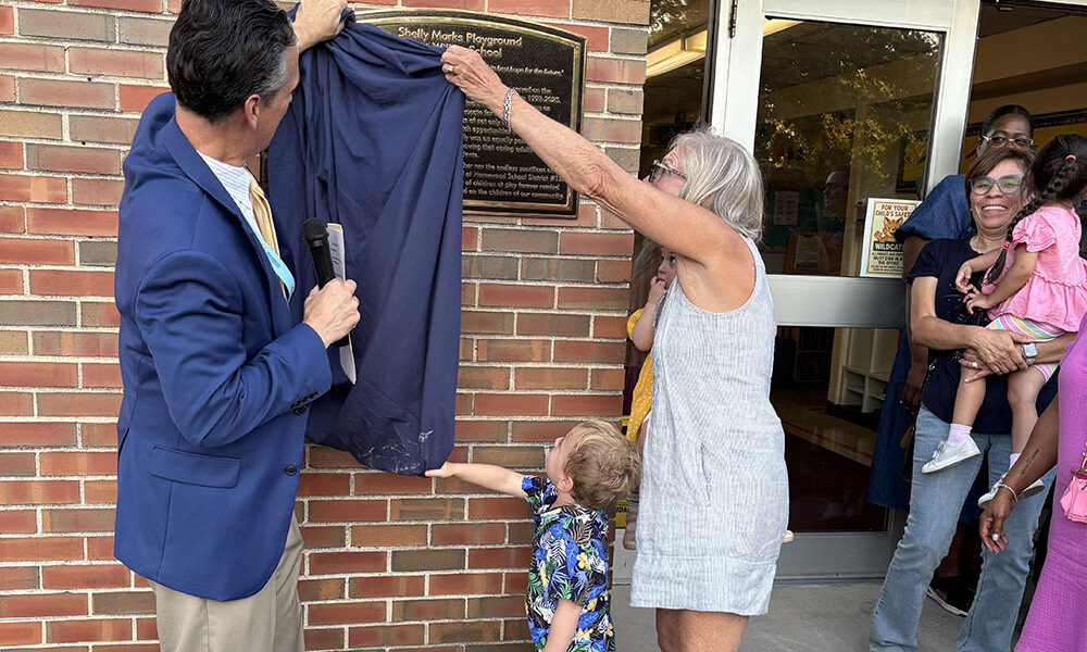 District 153 superintendent Scott McAlister helps Shelly Marks pull down the blue drape that unveils a plaque announcing the dedication of the playground at Willow School honoring her 32 years on the school board. (Marilyn Thomas/H-F Chronicle)