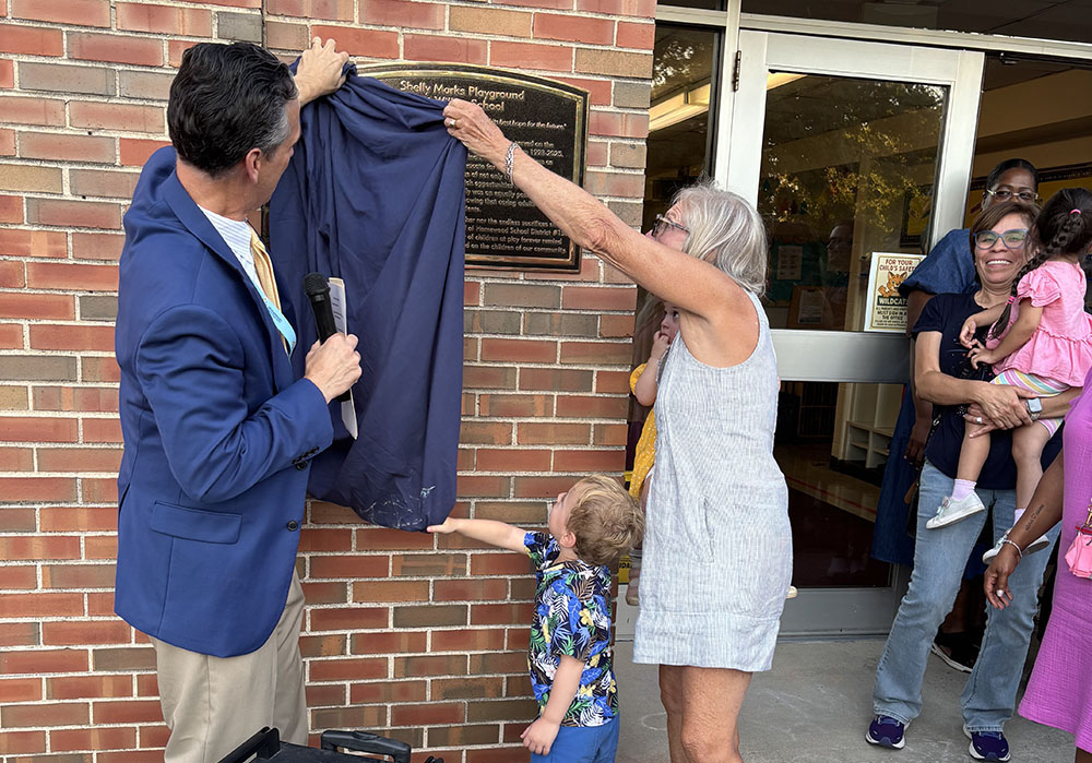 District 153 superintendent Scott McAlister helps Shelly Marks pull down the blue drape that unveils a plaque announcing the dedication of the playground at Willow School honoring her 32 years on the school board. (Marilyn Thomas/H-F Chronicle)