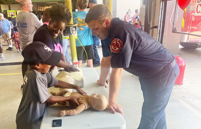 Flossmoor resident Karla Hughes learns the basics of CPR with her 7-year-old nephew, Aayyan Hughes, from Homewood firefighter and EMT Ryan Hope. (Nick Ulanowski / H-F Chronicle)