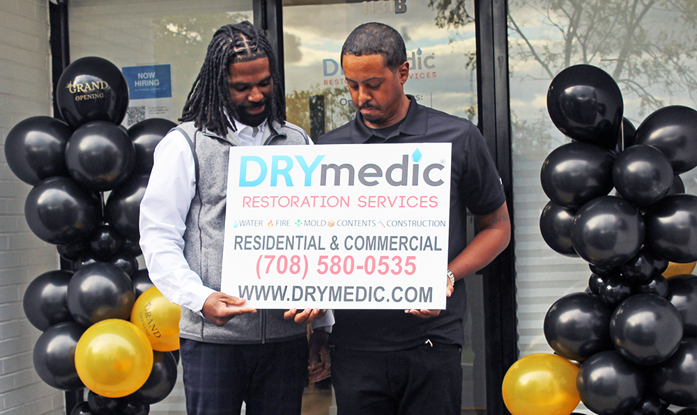 The cousins hold their new business sign after opening the Homewood location of DRYmedic Restoration Services. (Nuha Abdessalam/H-F Chronicle)