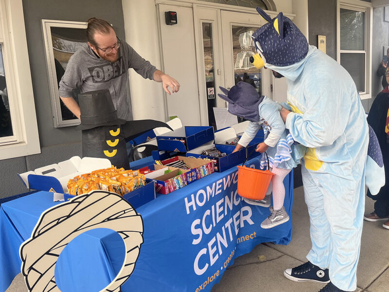 Chicago Heights residents Agustin Figueira, right, and his daughter Isabella Figueira get candy at the Homewood Science Center. Homewood Science Center STEAM educator Charlie Rohrer operates the booth. (Nick Ulanowski / H-F Chronicle)